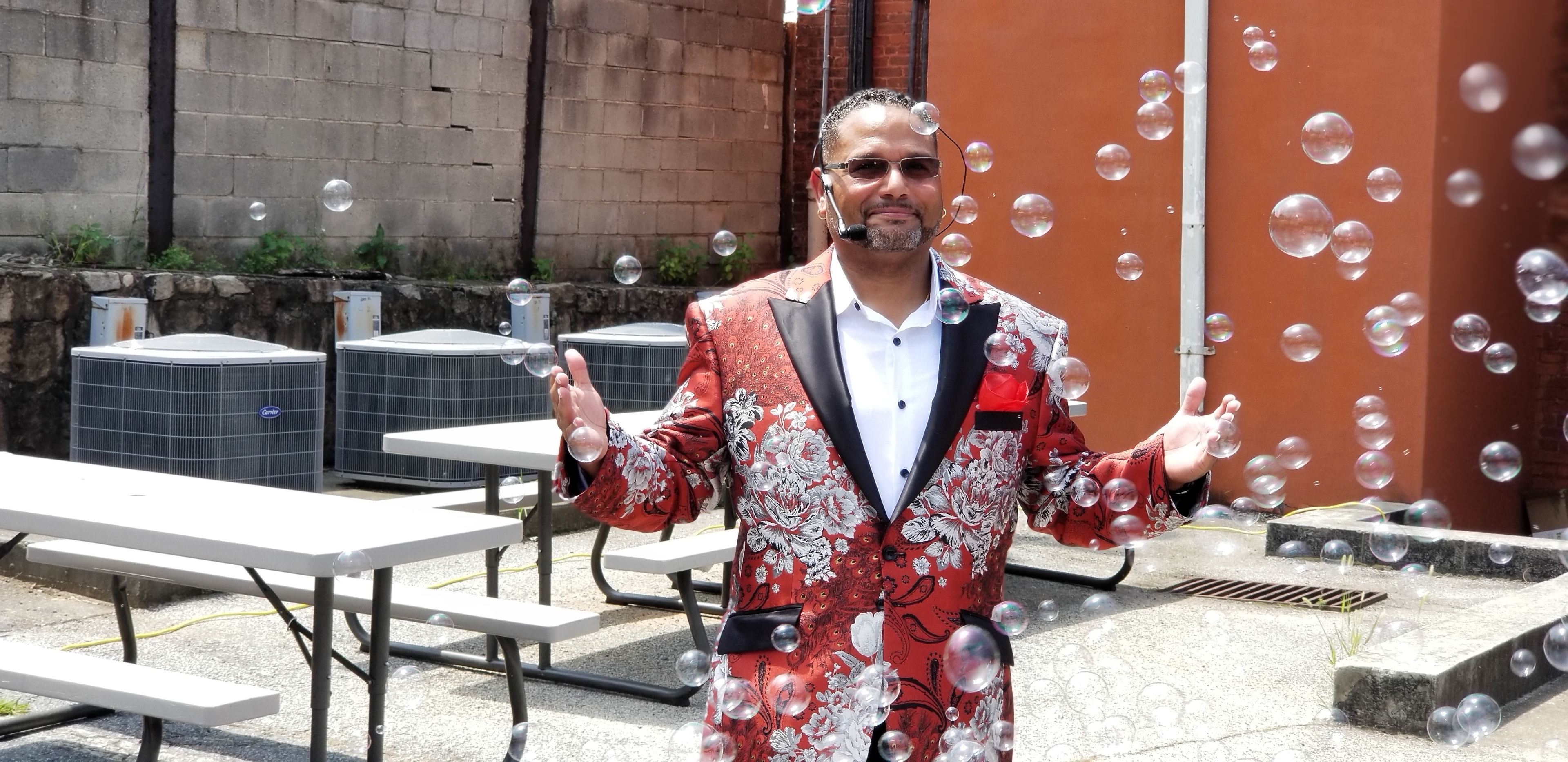 C. Magic performing outdoors in red floral blazer with bubbles